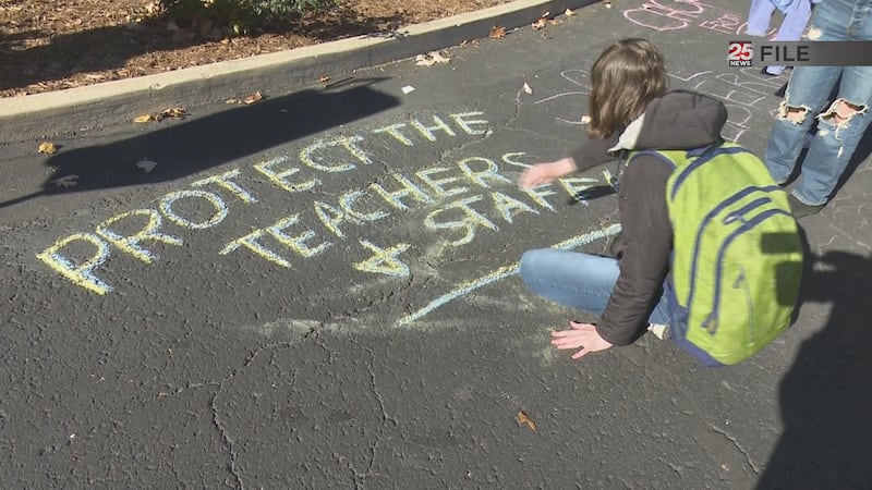 A student writes out chalk art during a campus walk out protesting the cuts.